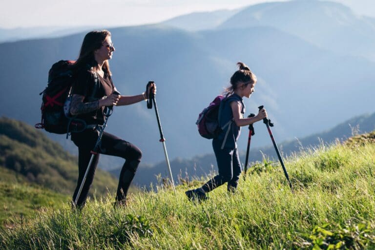 mother and daughter hiking uphill with trekking poles